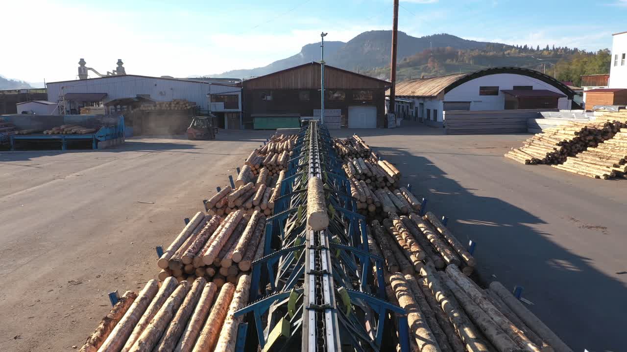 A POV drone flies forward along a log conveyor at an industrial sawmill. Raw timber is transported for processing, showcasing the supply chain and production in the wood industry