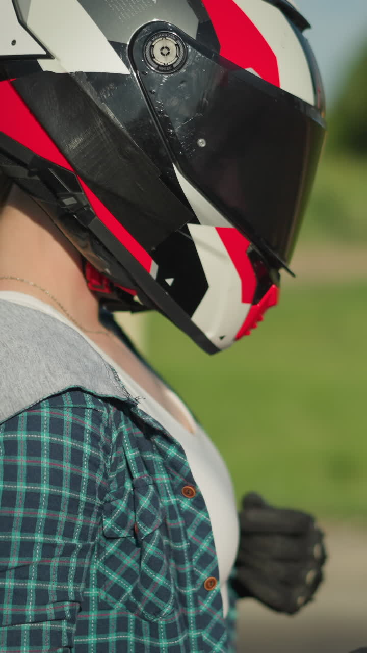 Close-up of a female biker adjusting her clothing while wearing a red-and-black helmet and black protective gloves