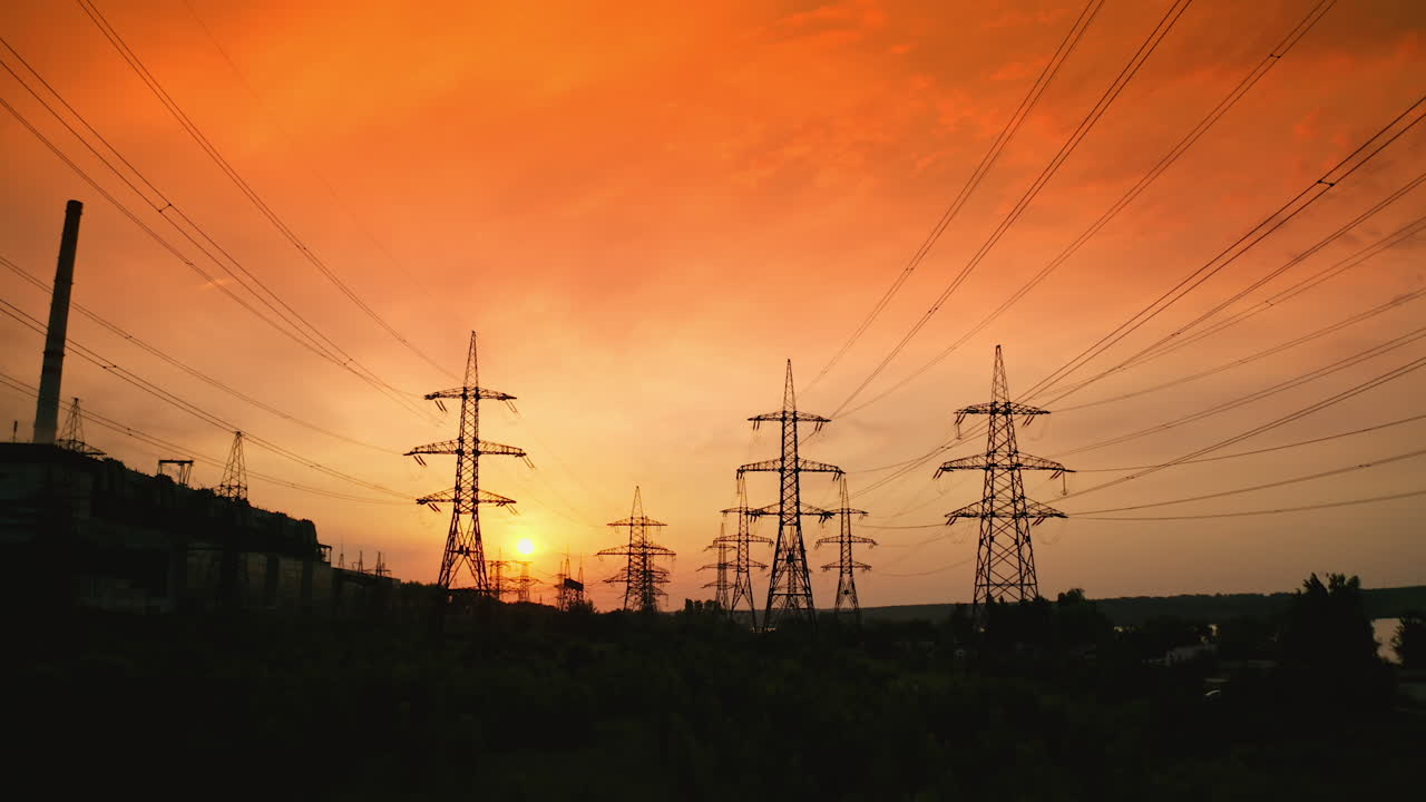 Dark silhouettes of electric towers on red sky background. Transmission lines of high-voltage electric towers at sunset.