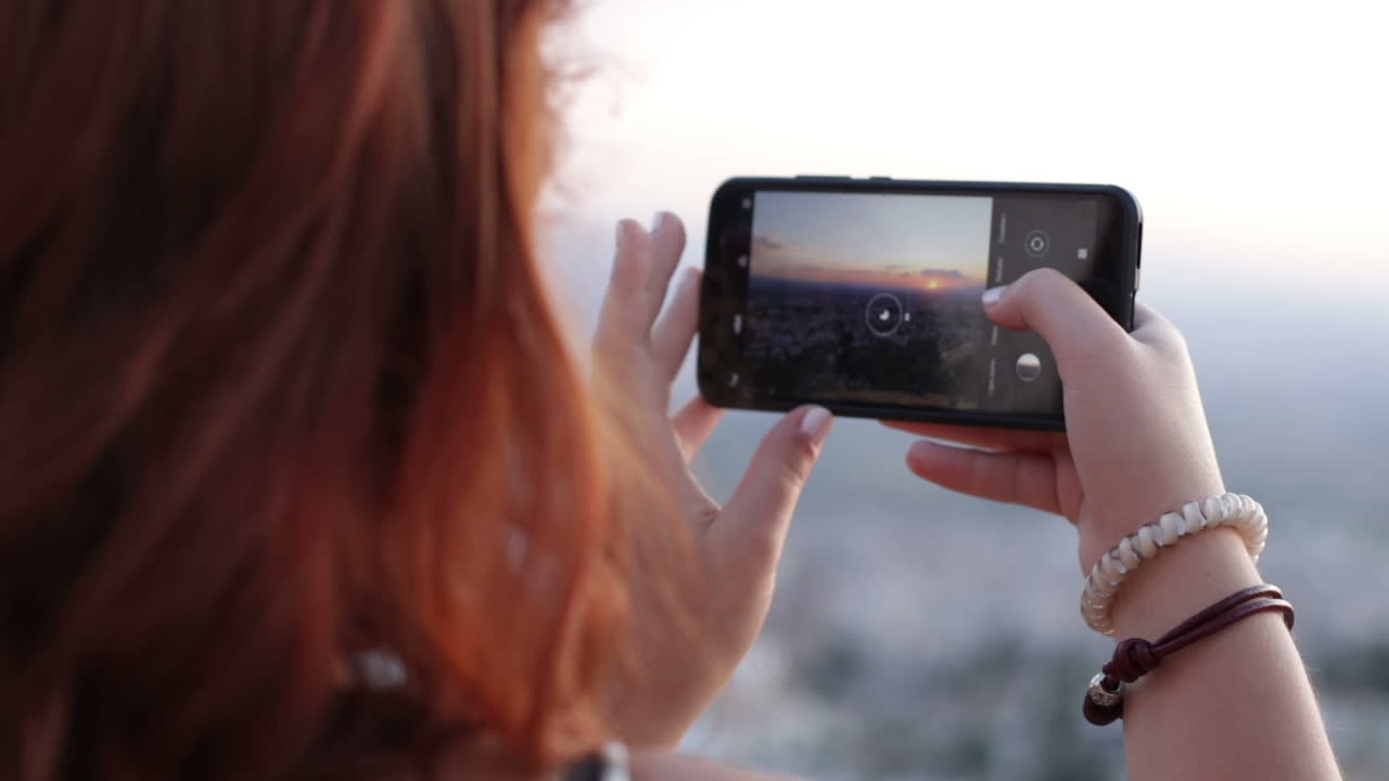 Woman taking a picture of a sunset cityscape with a smartphone