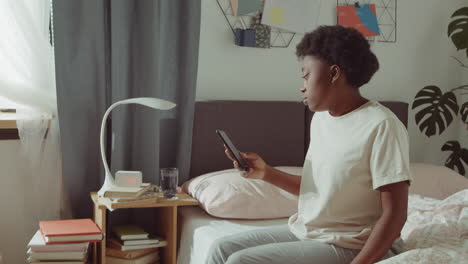 african american woman using phone on bed in morning