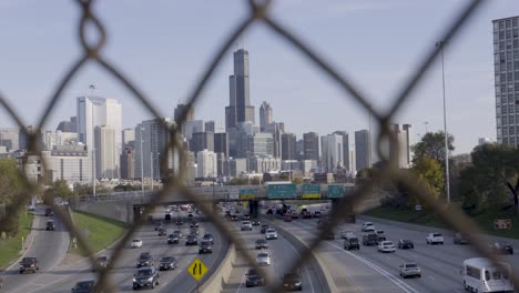 view of chicago's skyline and busy expressway through chain-link fence