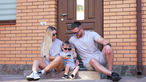 family having fun in the sun. a family of three sits on the steps of their house, smiling and enjoying a sunny day together with playful activities