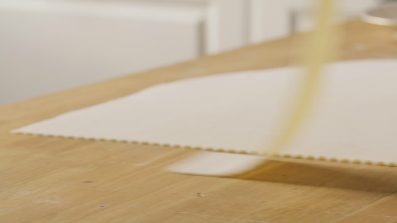 Lifting Freshly Cut Strip of Dough with Fluted Edges from Kitchen Table