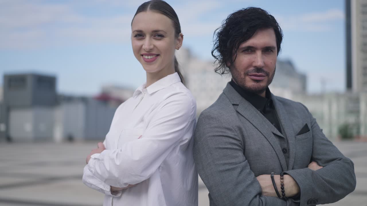 Live camera zoom in to confident satisfied successful couple crossing hands posing on city square. Young Caucasian man and woman looking at camera standing downtown. Slow motion.