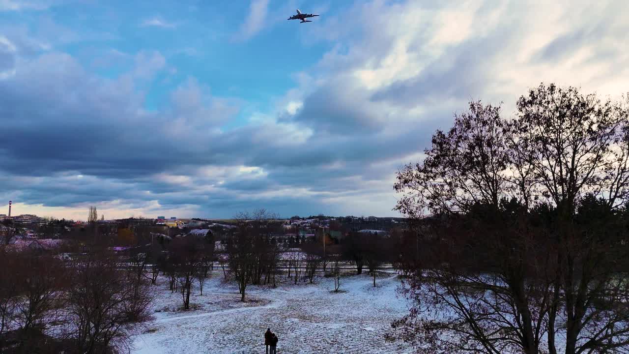 Person stand in snowy park with airplane crossing dramatic sky, Prague