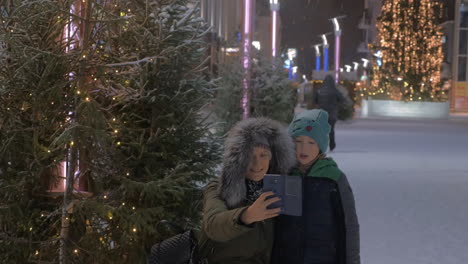 mom and kid making winter selfie in the street with christmas illumination