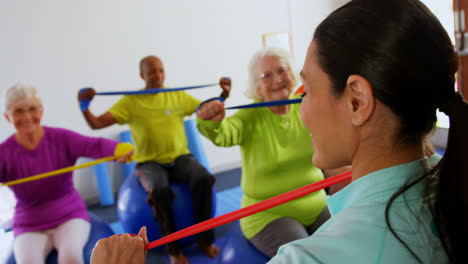 Rear-view-of-female-trainer-training-senior-people-in-exercise-at-fitness-studio-4k