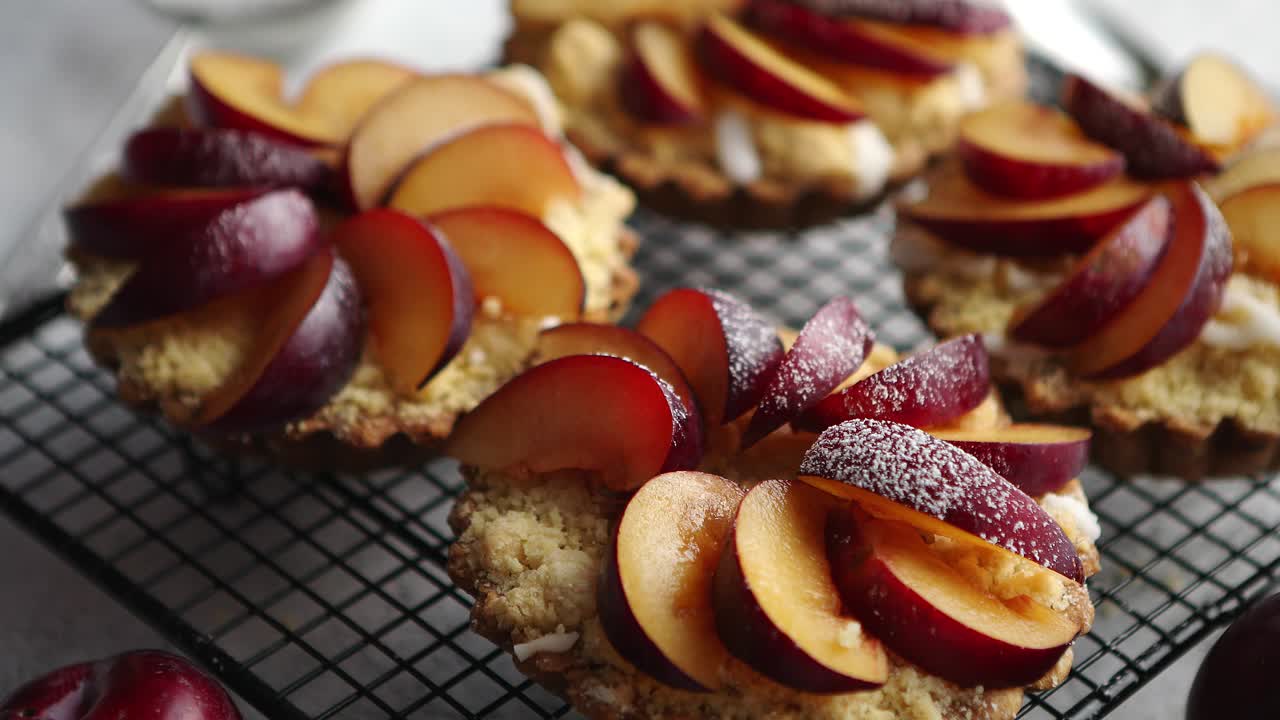 Homemade crumble tarts with fresh plum slices placed on iron baking grill