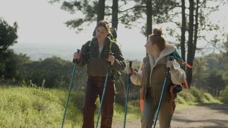 two young female backpackers hiking with trekking poles and talking in the forest on a sunny day 1