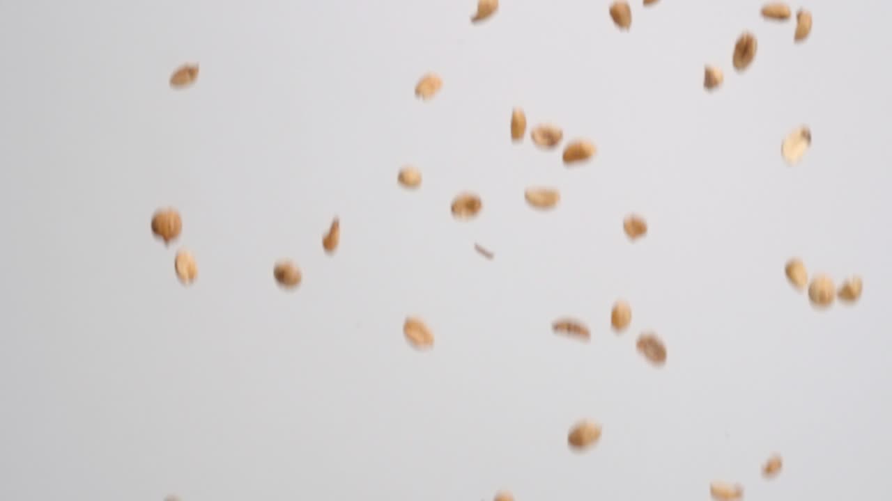 Salty roasted peanut snack raining down and bouncing on white backdrop in slow motion