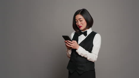 Front-desk-staff-in-uniform-looks-at-online-information-on-mobile-phone