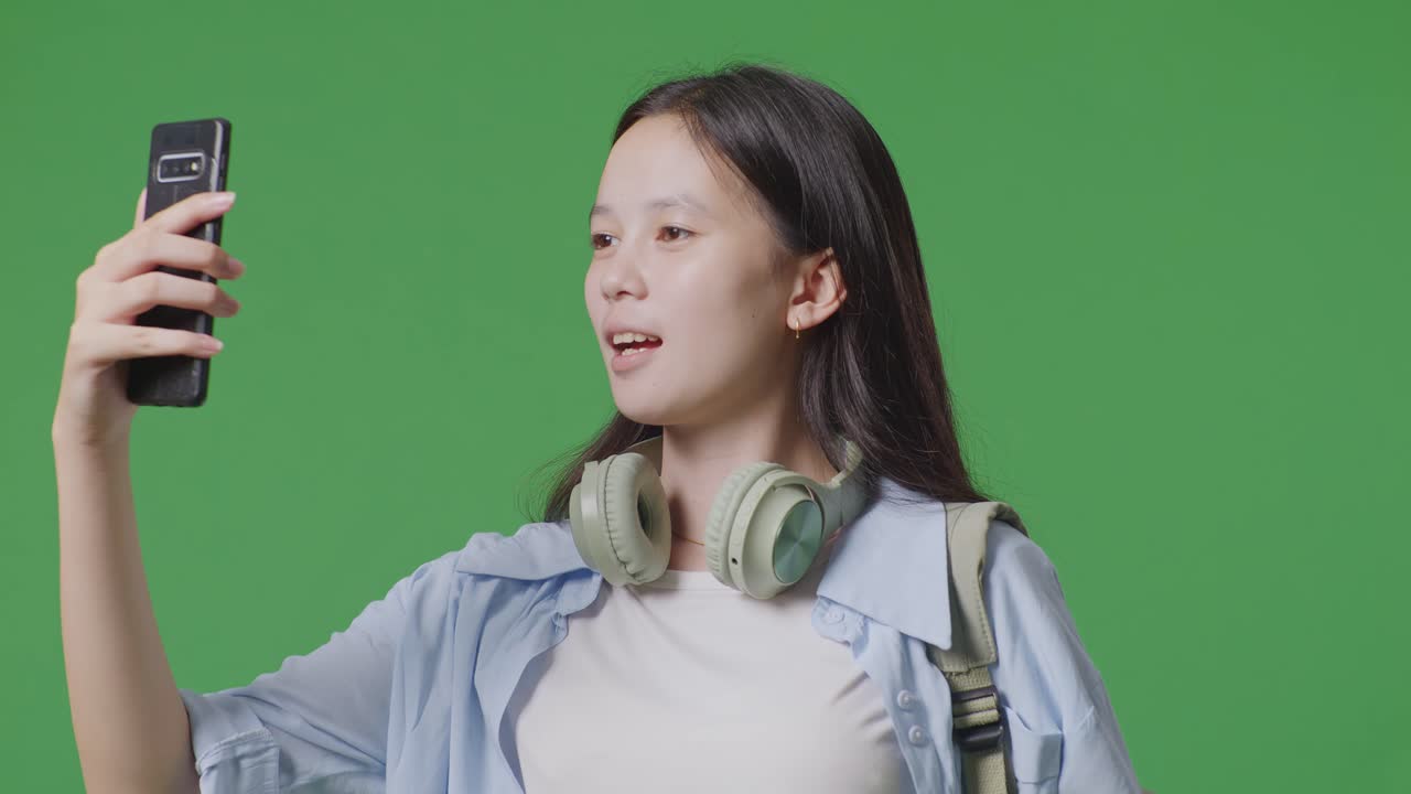 녹색 스크린 배경 스튜디오에 서 있는 스마트폰으로 비디오 통화를 하는 배을 가진 아시아 십대 소녀 학생의 클로즈업