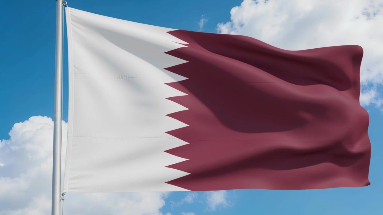 Bandiera del Qatar che sventola al vento su un'asta di metallo sotto un cielo azzurro limpido con nuvole