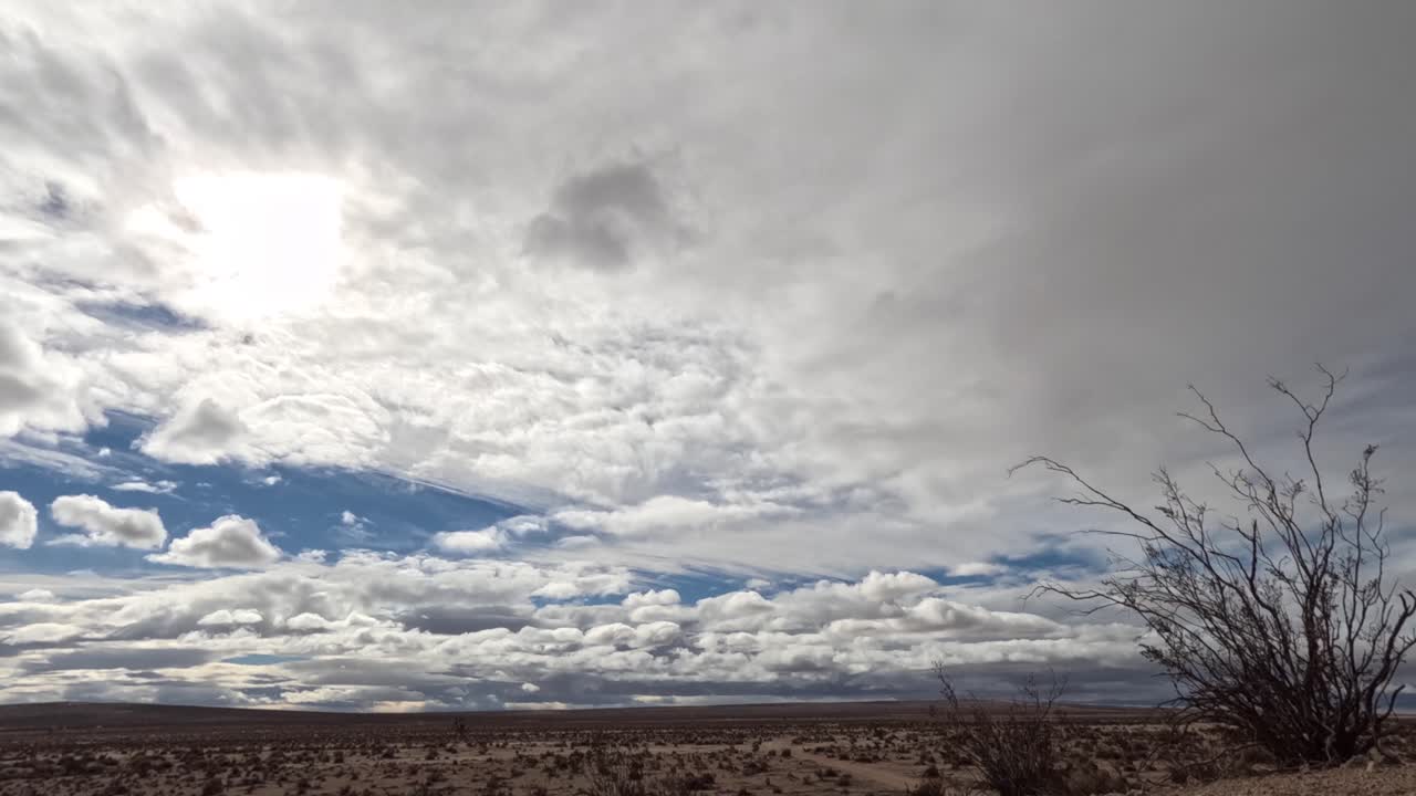 역동적인 클라우드스케이프 뒤에 태양 후광이 있는 모하비 사막 - 바람 부는 날의 시간 경과