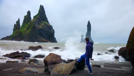 Hombre-Mirando-Las-Pilas-De-Mar-De-Reynisdrangar-Y-Las-Fuertes-Olas-De-La-Playa-De-Reynisfjara-En-El-Sur-De-Islandia