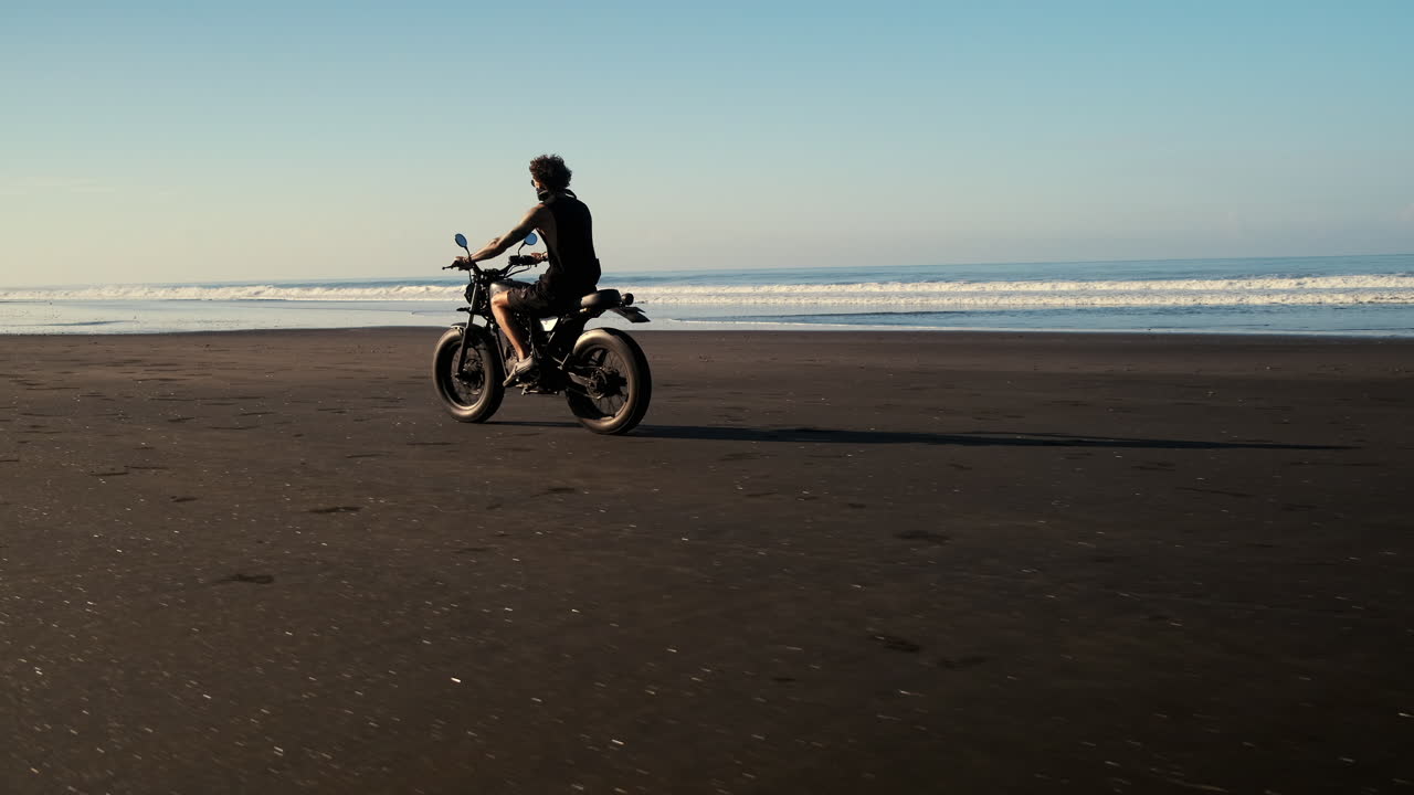 hombre montando una motocicleta en una playa de arena negra