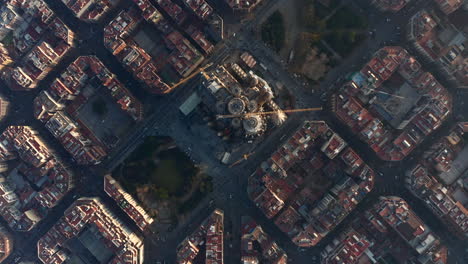 Fly-above-large-unfinished-church.-Top-down-shot-of-famous-basilica-Sagrada-Familia-and-surrounding-blocks-of-buildings.-Barcelona,-Spain