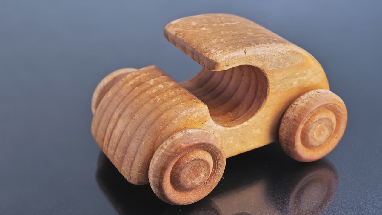 A hand places a rolled-up euro banknote into the trunk of a small, wooden toy car