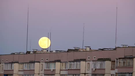 la gran luna llena sobre el techo de un edificio de varios pisos se está moviendo hacia arriba