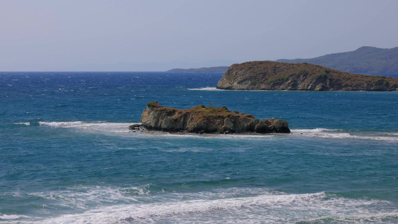 Vista costiera di isolotti rocciosi circondati dalle acque blu dell'oceano lungo la Costiera Amalfitana in Italia. Onde leggere si infrangono sotto il cielo sereno vicino a scogliere aspre