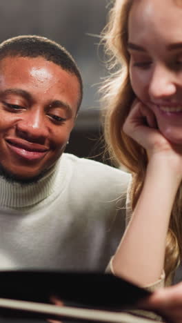 african-american bearded man turns page of photo album to introduce family to white woman colleague at table in sitting room closeup slow motion