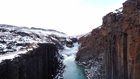 a captivating view within studlagil canyon reveals the serene turquoise river winding between towering walls of geometrically perfect basalt columns