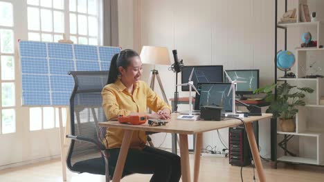 una mujer asiática feliz tiene éxito probando la turbina eólica mientras trabaja con una computadora portátil junto a la célula solar en la oficina