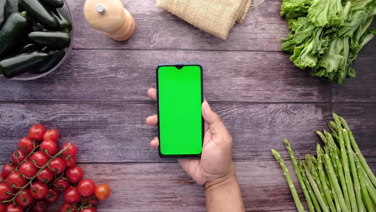 vista superior de la mano del hombre sosteniendo un teléfono inteligente con verduras frescas en la mesa
