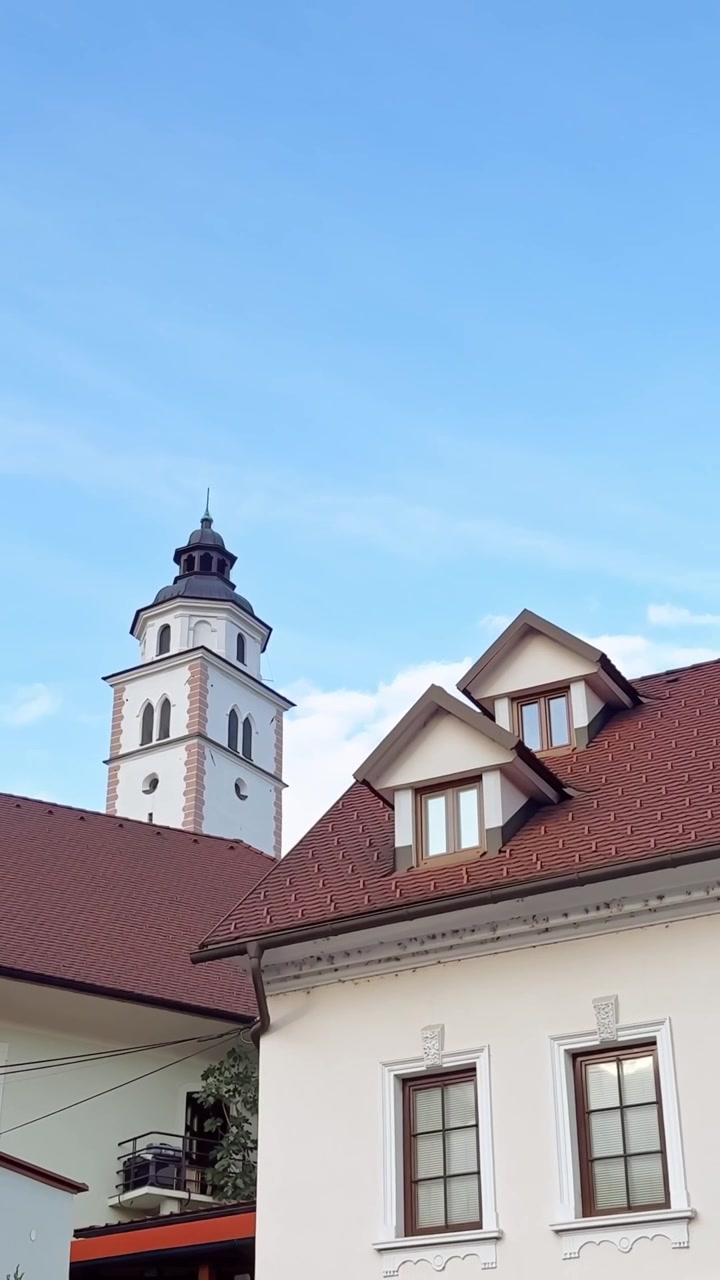 Torre della Chiesa del Rosario della Vergine Maria che si erge dietro i tradizionali tetti rossi nella storica Kranj, Slovenia, verticale