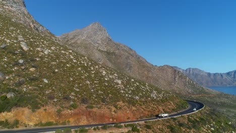 Aerial-drone-shot-of-land-rover-driving-off-on-a-mountain-pass-into-the-distant-as-the-view-pan-to-an-ocean-view