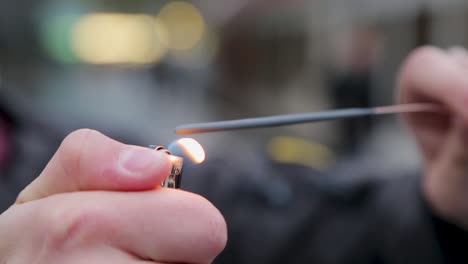 close-up of a sparkler being ignited by a person in blurred urban background