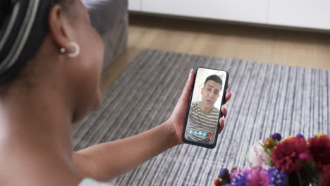 mujer biracial sosteniendo un teléfono inteligente con un hombre biracial con un sobre en la pantalla