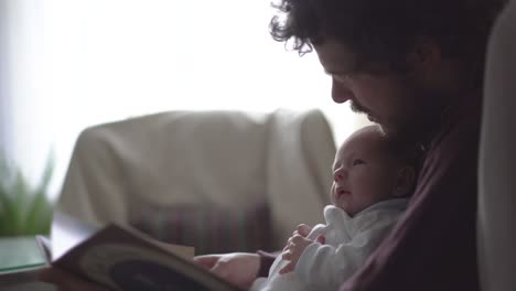 father with newborn baby reading book at home