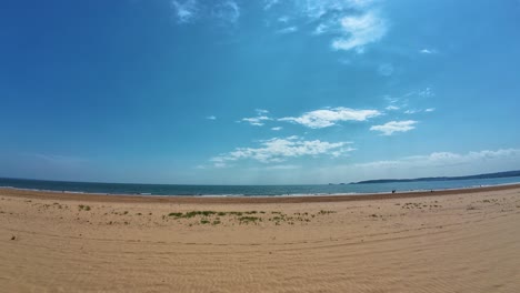 wide angle view of bright sunny day in summer of swansea bay with clean golden sands with mumbles pier in distance with calm waves rolling onto beach.