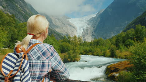 a female traveler looks at the beautiful mountains and glacier on top briksdal glacier in norway the