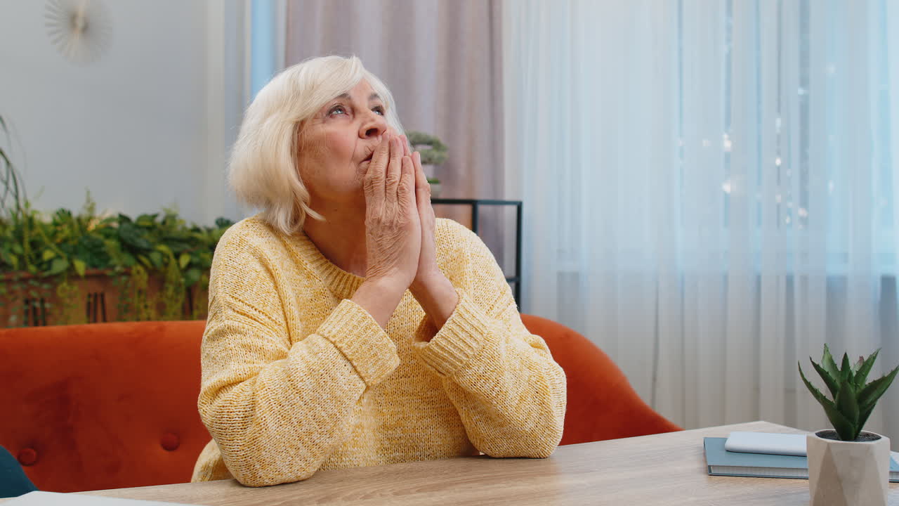 Worried senior elderly woman praying sincerely with folded arms asking god for help begging apology