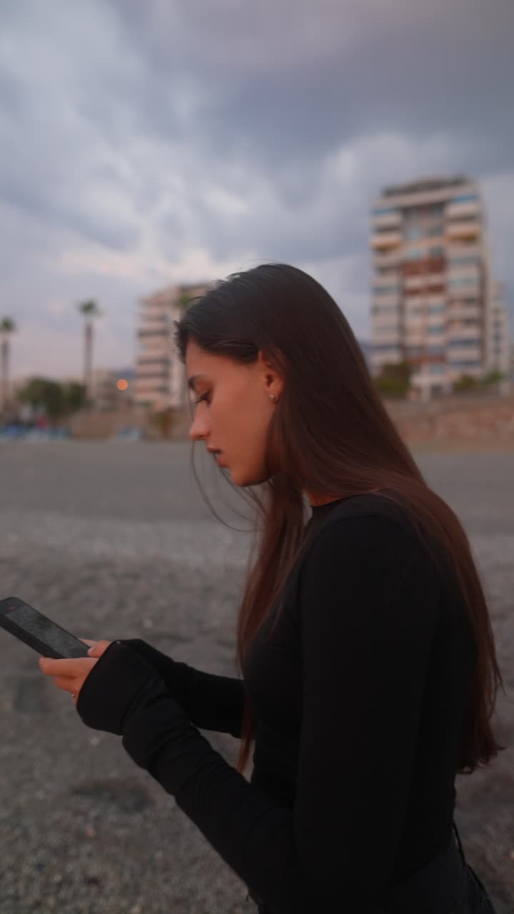 mujer mirando el teléfono en la playa al atardecer
