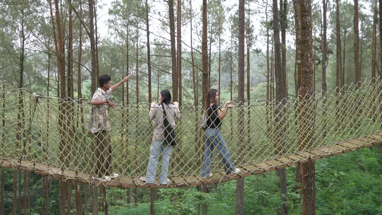 Young Asian Friends Crossing Rope Bridge in Forest Adventure
