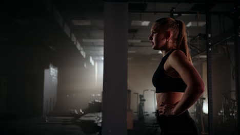 Mujer-Joven-Descansando-Después-De-Su-Entrenamiento-Y-Mirando-Hacia-Abajo.-Atleta-Femenina-Descansando-Después-Del-Entrenamiento-Físico-En-El-Gimnasio-Oscuro