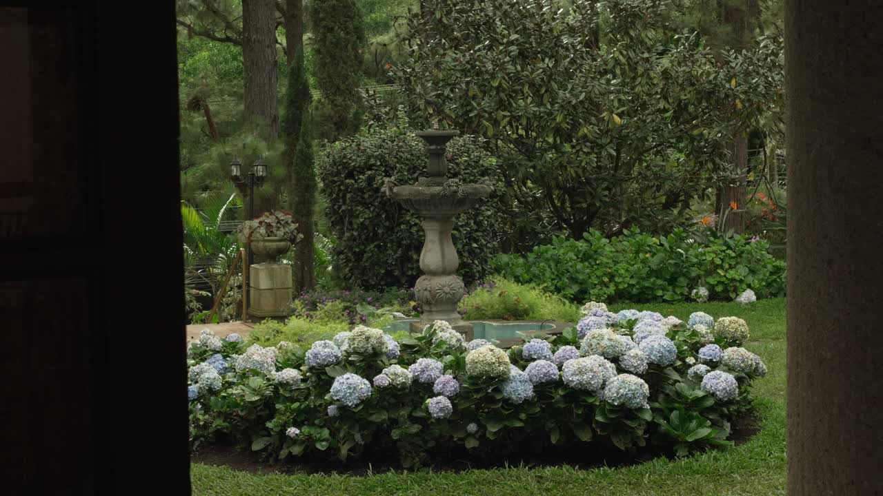 A beautiful garden with a fountain surrounded by flowers and green vegetation. Real estate.