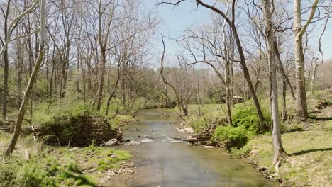 Aerial-view-of-natural-creek-flowing-in-spring-with-moving-water-through-trees-in-slow-motion