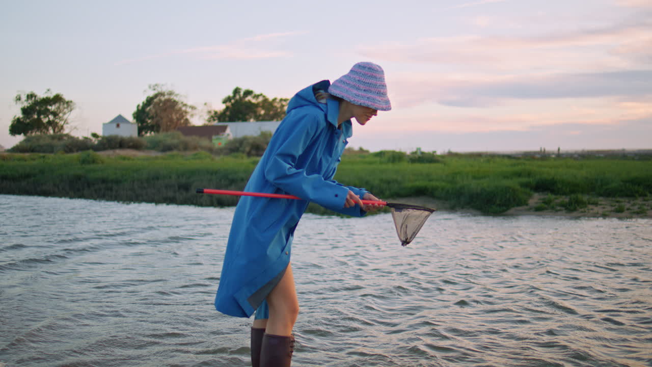девушка из деревни ловит рыбу на реке с сетью для бабочек вечером.