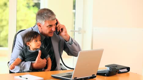 Man-holding-baby-and-answering-phone-at-desk