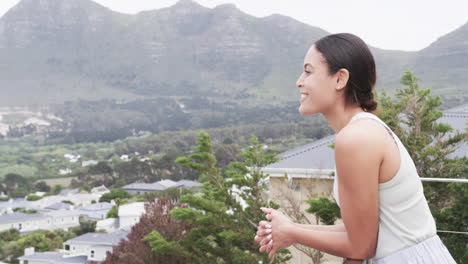 happy biracial woman standing on balcony looking away at home, copy space, slow motion