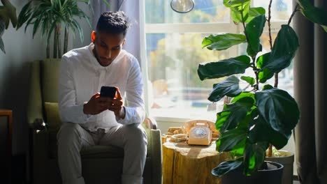 Front-view-of-young-asian-man-using-mobile-phone-in-living-room-at-home-4k