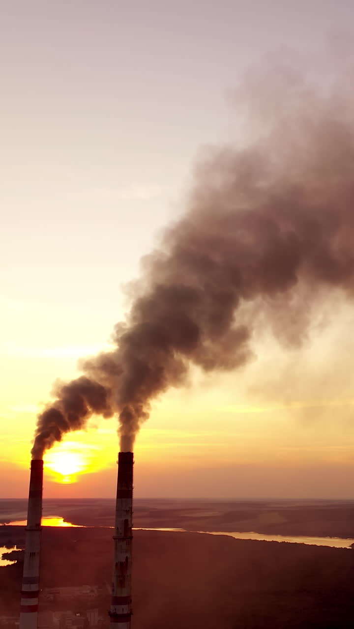 Pollution the atmosphere. Two factory pipes throw dirty emissions. Smoke looks beautiful but dangerous at sunset. Power plant on the beautiful landscape in the evening. Vertical video