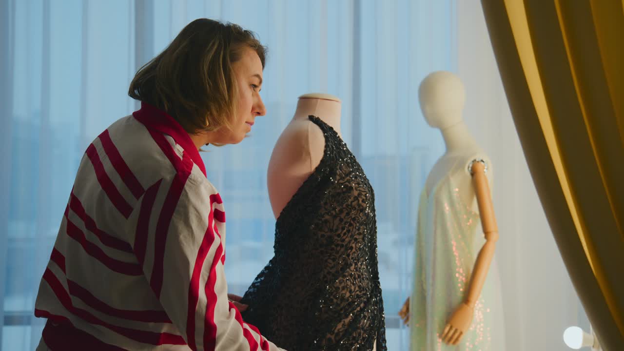 Woman carefully adjusts a black lace dress on a mannequin. She focuses intently, showing precision and care in her work. Natural light fills the space, creating a soft, professional atmosphere