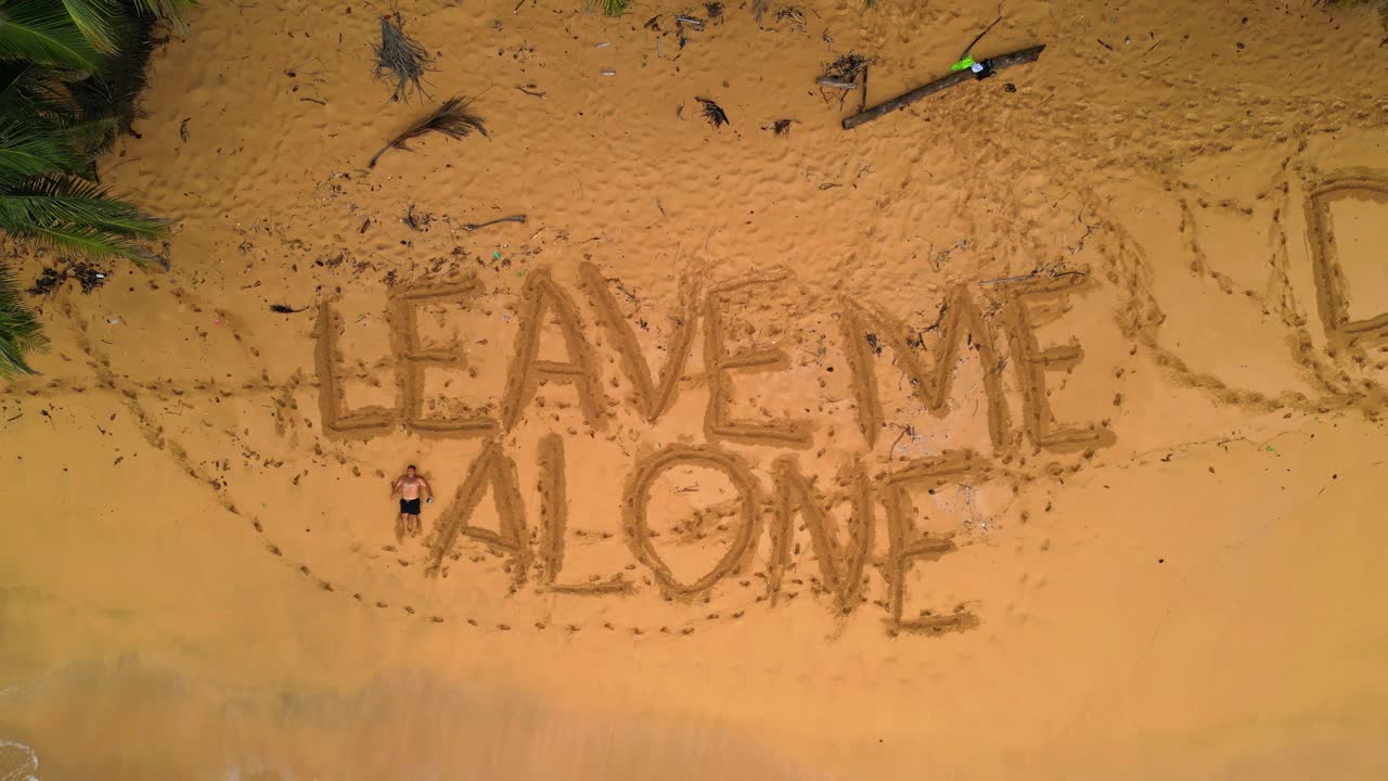 Aerial view of a desert beach with a man lying at sand next to the inscriptions in the sand saying Leave me Alone and Deixem me Aqui (Let me Here) in São Tomé,Africa. Ascendig drone shot