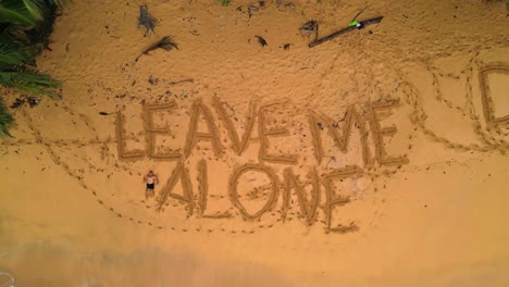 aerial view of a desert beach with a man lying at sand next to the inscriptions in the sand saying leave me alone and deixem me aqui (let me here) in são tomé,africa. ascendig drone shot